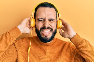 Sakallı, müzik dinleyen, kulaklık takan, dilini dışarı çıkaran, komik ifadeli genç bir adam.. 