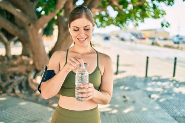 Genç sarışın sporcu şehirde bir şişe su içerek egzersiz yapıyor..