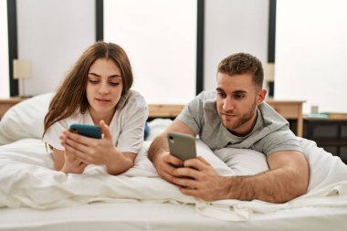 Kafkasyalı genç bir çift evde yatarken akıllı telefon kullanıyor..
