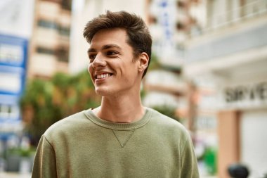 Genç İspanyol adam gülümseyerek şehirde mutlu mesut dikiliyor..