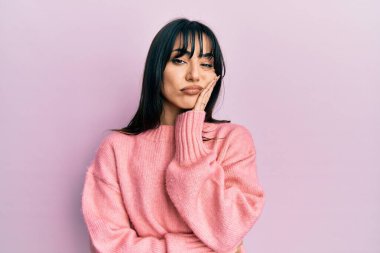 Kâküllü, kışlık süveter giyen genç esmer kadın kollarını kavuşturup depresyondan sıkılmış ve yorgun görünüyor.. 