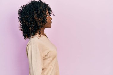 Afro-Amerikalı genç bir kadın, günlük giysiler içinde rahat bir görünüm takınıyor, doğal bir yüz ifadesi ve kendine güvenen bir gülümsemeyle poz veriyor.. 