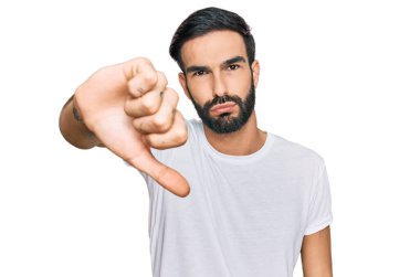 Gündelik beyaz tişört giyen genç İspanyol adam mutsuz ve kızgın görünüyor. Reddedilmiş ve olumsuz. kötü ifade. 