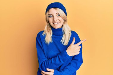 Genç beyaz kadın yün kazak ve kep giyiyordu. Gülümsüyordu. Elleri ve parmakları yan taraftaydı. 