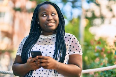 Genç Afrikalı Amerikalı kadın şehirde akıllı telefon kullanarak mutlu bir şekilde gülümsüyor..