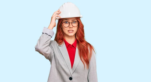 年轻的红头发女人戴着建筑师的硬礼帽 对问题感到困惑和好奇 拿不定主意 手拿着头思考 沉思的概念 — 图库照片