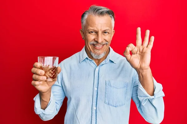 Średniowieczny Siwowłosy Mężczyzna Pijący Szklankę Whisky Robi Znak Palcami Uśmiechnięty — Zdjęcie stockowe