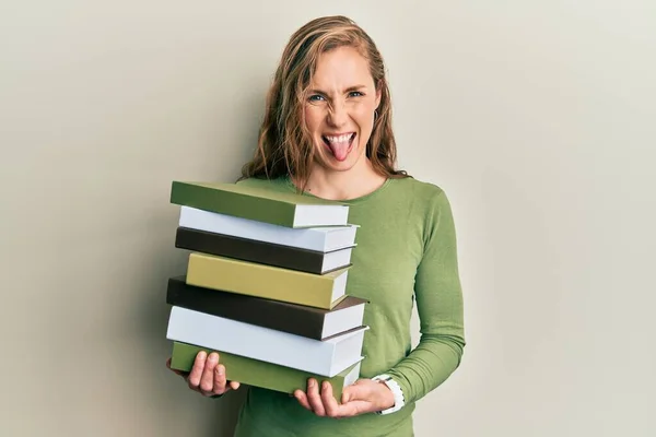 年轻的金发女人拿着一堆书 带着滑稽的表情高兴地伸出舌头 — 图库照片