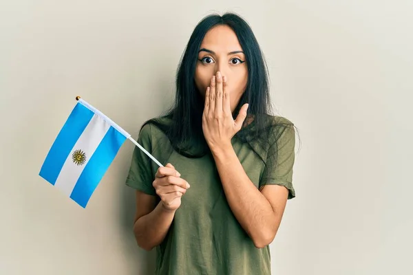 Jovencita Hispana Sosteniendo Bandera Argentina Cubriendo Boca Con Mano Conmocionada —  Fotos de Stock