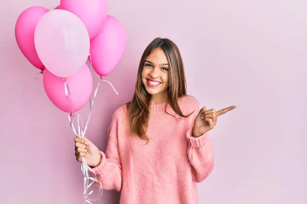 stock image Young brunette woman holding pink balloons smiling happy pointing with hand and finger to the side 