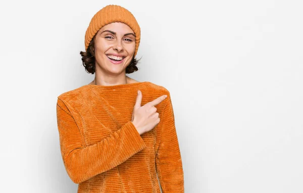 カジュアルな服とウールキャップを身に着けている若いヒスパニック系の女性は 顔に幸せと自然な表情で側に手と指で指して笑顔で陽気にキャップ — ストック写真