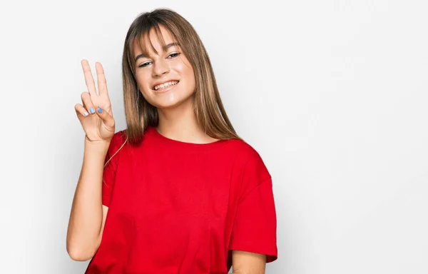 十几岁的女孩穿着休闲的红色T恤 喜形于色地微笑着 用手指在镜头前眨眼示意胜利 第二点 — 图库照片