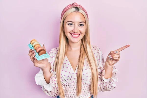 Menina Loira Jovem Segurando Deliciosos Macarons Doces Sorrindo Feliz Apontando — Fotografia de Stock