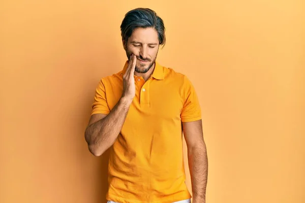 歯痛や歯の病気のために痛みを伴う表現で手に触れるカジュアルな黄色のTシャツを身に着けている若いヒスパニック系の男 歯科医 — ストック写真