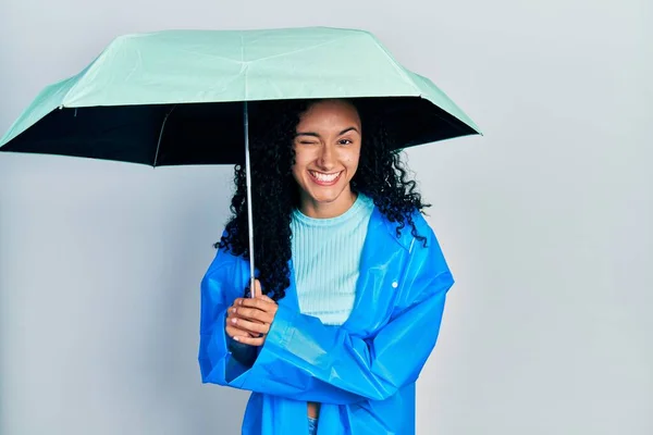 年轻的惊慌失措的女人 卷曲的头发 穿着雨衣 带着雨伞眨眼 带着性感的表情 笑容满面地看着相机 — 图库照片