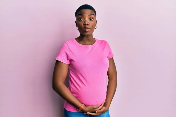 赤ちゃんを期待している若いアフリカ系アメリカ人女性は 狂気とコミカルなジェスチャーで魚の顔を作る妊娠中の腹に触れます 面白い表現 — ストック写真