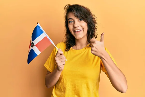 年轻的惊慌失措的女人举着多明尼加共和国的国旗 高兴而积极地微笑着 竖起大拇指做得很出色 签了字 — 图库照片