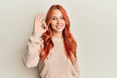 Genç, güzel, kızıl saçlı, sıradan bir kazak giyen, gülümseyen, el ve parmaklarıyla 