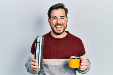 Sakallı yakışıklı beyaz adam bir fincan kahve içiyor termo tutuyor ve kahkahalarla gülüyor.. 