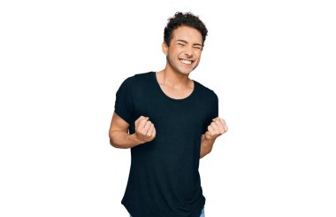 Başarılı olmak için heyecanlı, kolları havada ve gözleri kapalı zaferi kutlayan siyah tişört giyen genç yakışıklı bir adam. Kazanan konsept. 