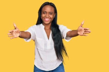 Sıradan kıyafetler giyen genç siyahi kadın kameraya sarılıp gülümseyerek gülümsüyor. Mutluluğu kucaklayan neşeli bir ifade.. 