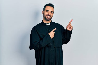 Sakallı yakışıklı, Katolik rahip cübbesi giyen, gülümseyen ve kameraya bakan iki eli ve parmakları yanda olan İspanyol bir adam.. 