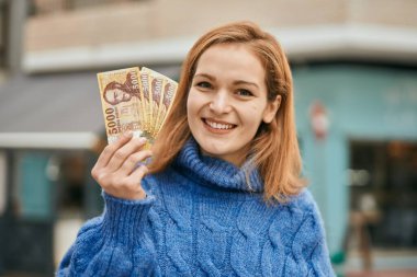 Genç beyaz kız mutlu bir şekilde gülümsüyor. Şehirde Macar banknotları tutuyor..