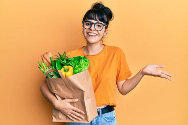 Genç İspanyol kız, elinde ekmek ve bakkaliyeyle kağıt torba tutarak başarıyı mutlu bir gülümsemeyle ve kazanan ifadeyle kutluyor. 