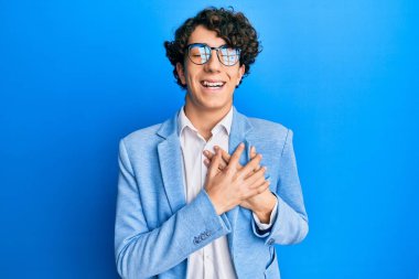 İş ceketi giyen, gözlüklü, elleri göğsünde, gözleri kapalı gülümseyen ve yüzünde minnet ifadesi olan İspanyol bir genç. sağlık kavramı. 