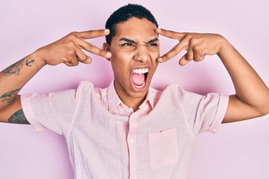 Genç Afro-Amerikalı adam zafer işareti yapıyor ve barış hareketi yapıyor kızgın ve öfkeli çığlıklar atıyor, öfkeyle bağırıyor. öfke ve agresif konsept. 