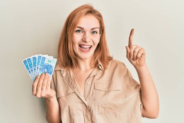 Elinde 50 Polonyalı zloti banknotla gülümseyen genç beyaz kadın bir fikir veya soru işareti ile mutlu bir yüzle, bir numara 