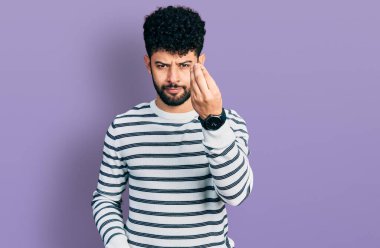 Sakallı, sıradan çizgili süveter giyen, el ve parmaklarıyla italyan jestleri yapan genç bir Arap. 