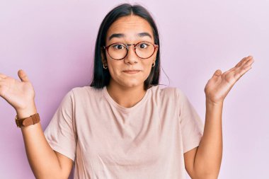 Sıradan kıyafetler ve gözlük takan genç Asyalı kadın habersiz ve kolları açık, hiçbir fikri yok ve şüpheli bir yüzü var.. 