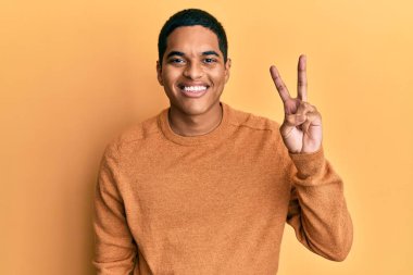 Genç, yakışıklı, sıradan bir süveter giyen, iki numaralı parmağını gösterip gülümseyen, kendinden emin ve mutlu bir İspanyol.. 