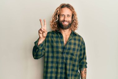 Sakallı, uzun saçlı, sıradan kıyafetler giyen, iki numaralı parmaklarıyla işaret eden, kendinden emin ve mutlu bir adam.. 