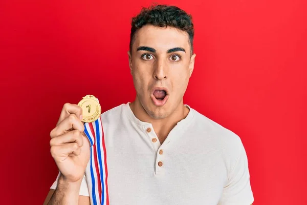 Jovem Hispânico Segurando Medalha Primeiro Lugar Assustado Espantado Com Boca — Fotografia de Stock