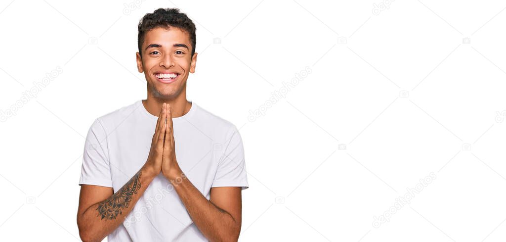 Young handsome african american man wearing casual white tshirt praying with hands together asking for forgiveness smiling confident. 