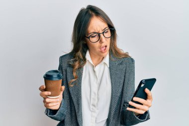 Genç esmer kadın akıllı telefon kullanıyor ve şok olmuş bir şekilde bir fincan kahve içiyor. Şüpheci ve alaycı görünüyor. 