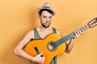 Latin asıllı genç bir adam klasik gitar çalıyor cahil ve kafası karışık bir ifade. şüphe kavramı. 