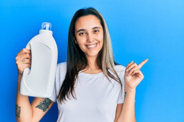 Deterjan şişesini tutan genç İspanyol kadın gülümsüyor. 