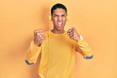 Kulaklıkla müzik dinleyen Afro-Amerikalı genç adam kızgın ve kızgın yumruklar sallarken öfkeyle bağırıyor. öfke ve agresif konsept. 