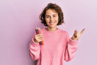 Genç esmer kadın elinde renkli kalemlerle gülümsüyor mutlu bir şekilde elini ve parmağını yana doğru uzatıyordu. 