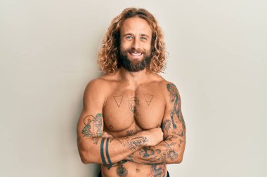 Sakallı, uzun saçlı, dövmeleri olmayan, kolları çaprazlanmış gülümseyen ve kameraya bakan yakışıklı bir adam. pozitif kişi. 