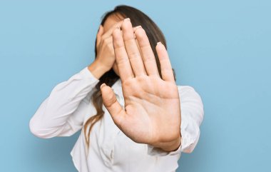 Genç esmer kadın gündelik giysiler giyip ellerle gözlerini kapatıyor ve üzgün ve korku ifadeleriyle jest yapıyor. utangaç ve olumsuz kavram. 