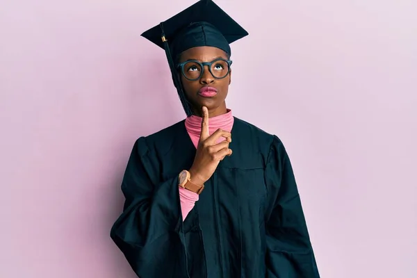 졸업식 모자를 예복을 아프리카 미국인 소녀는 손가락을 올려다보며 의심에 집중적으로 — 스톡 사진