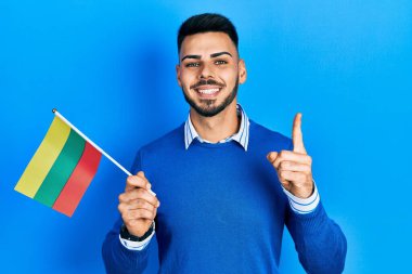 Litvanya bayrağı tutan sakallı genç İspanyol bir adam bir fikir veya soruyla gülümsüyor ve mutlu bir yüzle işaret ediyor. 