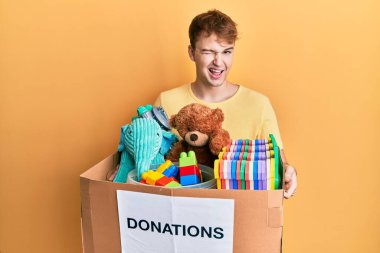 Elinde oyuncaklarla bağış kutusu tutan beyaz bir adam kameraya seksi bir ifadeyle bakıyor, neşeli ve mutlu bir yüz.. 