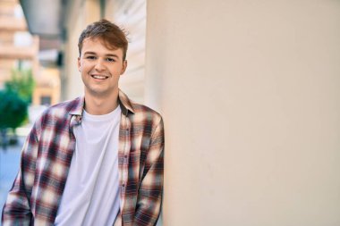 Genç beyaz adam gülümseyerek şehirde mutlu mesut duruyor..