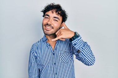 Günlük kıyafetler giymiş, gülümseyen genç İspanyol adam telefonla el ve parmak hareketleri yapıyor telefonda konuşur gibi. iletişim kavramları. 