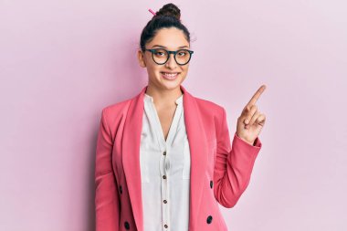 Orta Doğulu güzel bir kadın iş ceketi ve yüzünde kocaman bir gülümseme olan gözlüklerle kameraya el ile işaret ederek bakıyor.. 